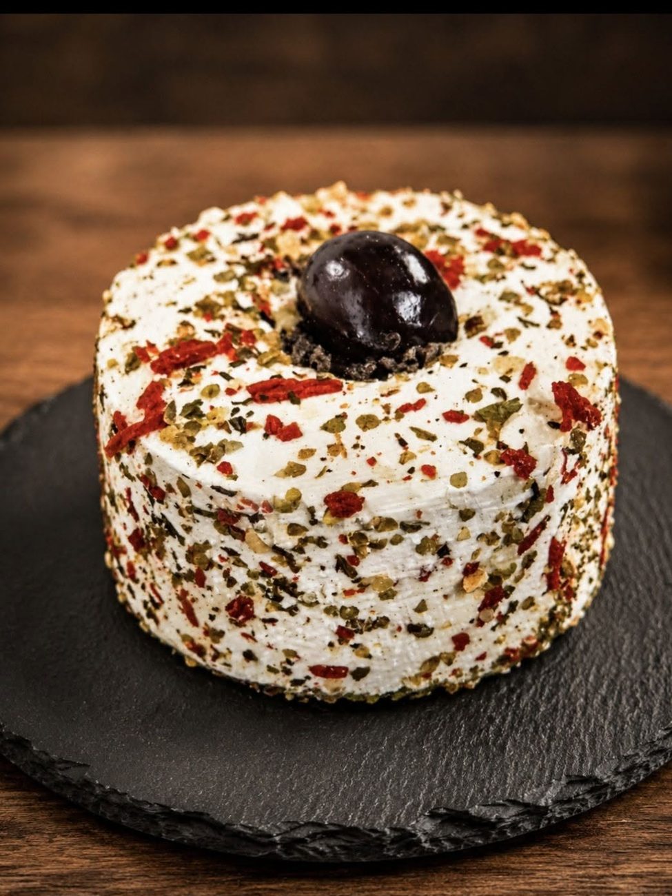 Spécialité au fromage de chèvre enrobée de poivres et d'herbes, surmontée d'une olive